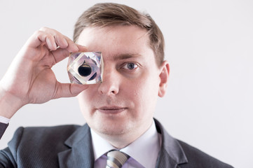 Fototapeta premium Businessman in suit and tie holds in hands and looks to the drop of black oil of Brent brand in crystal cube. Crisis in financial market, falling and rising prices, quotes, changes in exchange rate