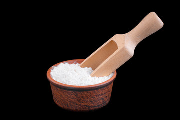 Clay bowl with flour and wooden scoop isolated on a black background.