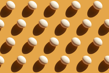 Repeating white eggs with a hard shadow on a beige yellow background, easter background in pop art style