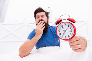 Wake up early every morning. Health benefits of rising early. Waking up early gives more time to prepare and be timely. Hipster bearded man in bed with alarm clock. Time to wake up. Healthy habits