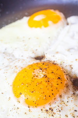 Fried egg close-up: whole yolk in focus. The concept of fried food, breakfast. Egg sprinkled with pepper.