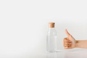 Hand with thumb up next to a glass bottle with clear water.