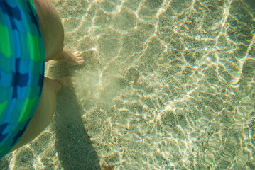Naklejka na ściany i meble Bare feet of a girl in transparent clear water. Top view