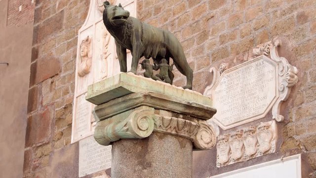 Statue of she-wolf on Capitoline hill against red brick wall. Twins founders of Rome city - Romulus and Remus - suckling she-wolf. Icon of Italian capital Rome city. Camera moving up