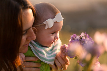 A mother and her baby stop and smell the flowers on an outdoor hike.