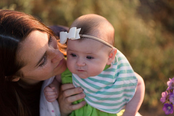 A mother and her baby stop and smell the flowers on an outdoor hike.
