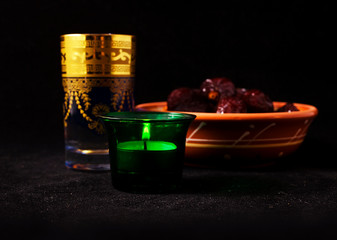 Ramadan lamp and dates with a glass of water, still life on a black background.