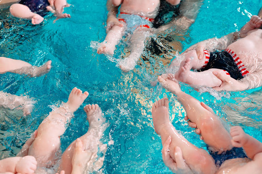 A group of mothers with their young children in a children's swimming class with a coach.