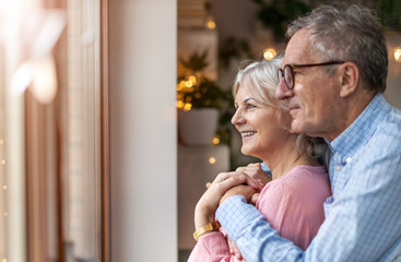 Mature couple looking out through window at home