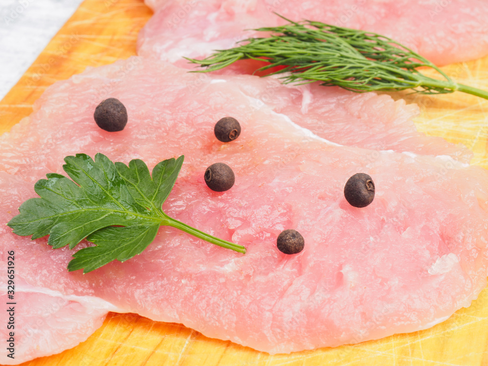 Wall mural Sliced pieces of meat turkey game filet on a wooden cutting board, herbs, allspice. Healthy eating concept