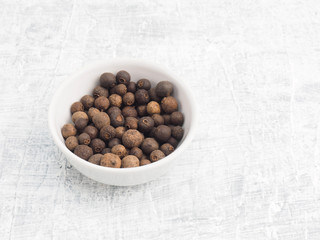 Spice allspice pepper in white ceramic bowl on a white concrete background. Indian cuisine,...
