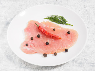 Sliced pieces of meat turkey game filet on white ceramic plate, allspice, red chili pepper, fennel on concrete background. Healthy eating concept