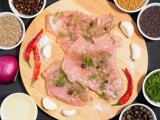 Sliced pieces of meat turkey game filet on a wooden cutting board, garlic, salt, fennel, allspice, red chili pepper, red onion, cumin, cloves, oil, mustard seeds. Healthy eating concept