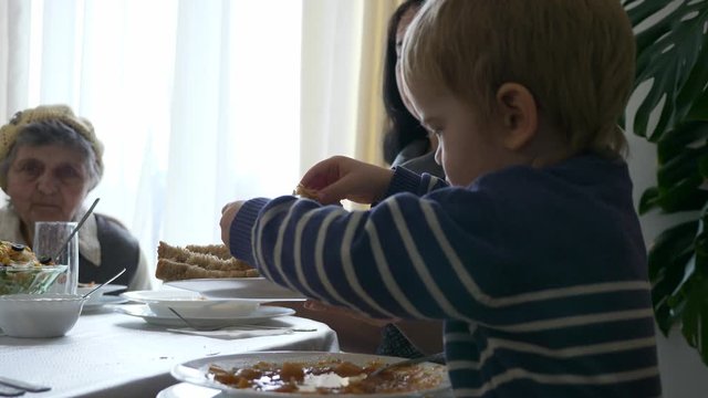 Little Child Takes Piece of Bread and adds in Soup. Multi Generation Family Having Dinner Enjoying Meal. Slow motion 0.5 speed 60 fps
