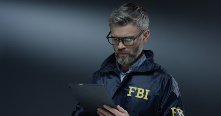 Good looking Caucasian grey-haired male FBI policeman in glasses tapping and scrolling on the...