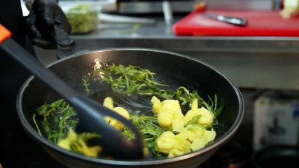 Close up slow motion of stirring homemade tortelini pasta in a frying pan with melted butter and arugula leaves - Powered by Adobe