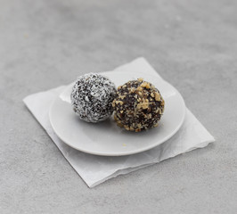 Vegan energy balls made from dried prunes, dates, dried apricots and almonds, cashews, walnuts, with nut and coconut topping on a plate on a light background