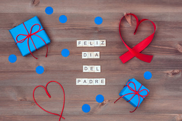 Feliz dia del padre words made of wooden blocks with blue gift boxes and red hearts on wooden background. Happy fathers day greeting card, holiday flat lay, top view