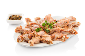 Raw chicken drumstick, marinating in a seasoned sauce, before cooking. On a ceramic plate, with seasoning on a ramekin aside. Isolated on white background.