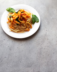 Pasta with squid and spinach in tomato sauce in a white plate on a neutral background. Gray background. Space for text. Copy space. Vertical orientation. For restaurant menus