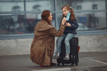 A European mother in a respirator with her daughter are standing near a building.The parent is teaching her child how to wear protective mask to save herself from virus.