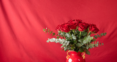 Beautiful bouquet of red roses in a red vase on the red background with copy space.