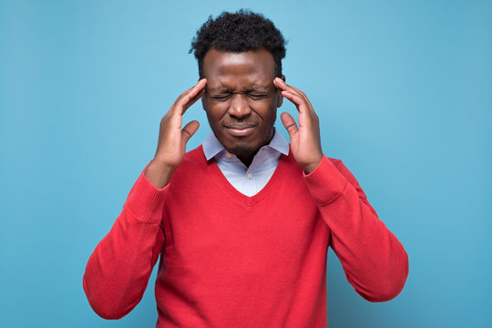 Serious afro american man in red sweater with headache in studio on blue isolated background