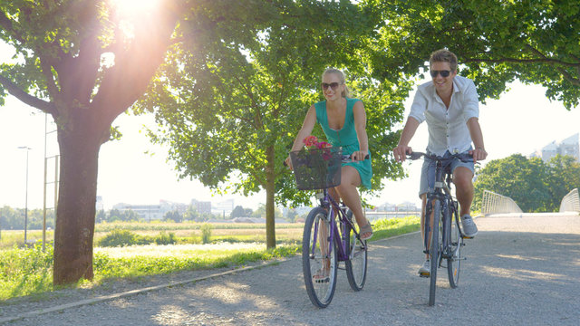 LENS FLARE: Cinematic shot of a couple riding their bikes along a sunlit avenue.