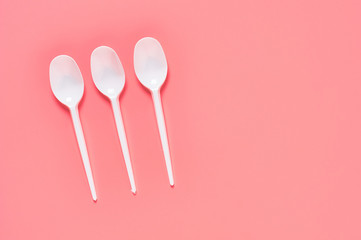 Row of white disposable spoons scattered on pink background. Concept of save environment, ecology,...
