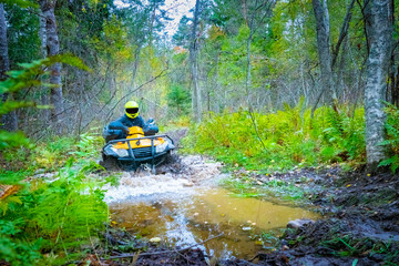 ATV rides in a large puddle. Dirt ride on an ATV. Biker rides through the woods. Concept - extreme off-road racing. Overcoming obstacles in the forest. Concept - quad bike rental. ATV Driving Courses