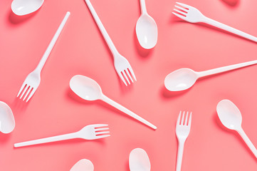 White disposable spoons and forks scattered on pink background. Concept of save environment,...