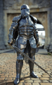 Powerful medieval knight standing with a full suit of armor and holding a sword weapon in front of his castle. 3d rendering