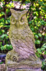 Old owl stone sculpture in a garden.