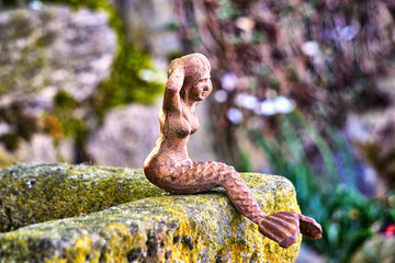 Sculpture of a little mermaid on a natural stone as a garden decoration.