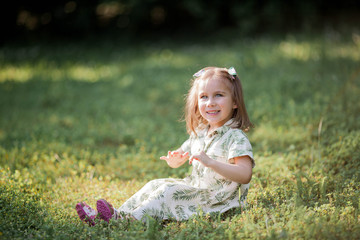 Little cute girl is sitting on the grass. Happy girl in the park. Summer.