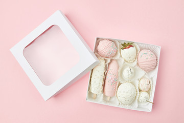Gift box with ripe fruits covered with white and pink chocolate lies on a pink background