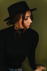 Beautiful girl in black golf and a black hat with gold earrings on an olive background