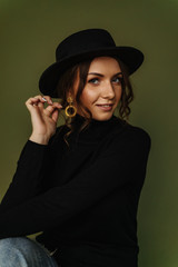 Beautiful girl in black golf and a black hat with gold earrings on an olive background