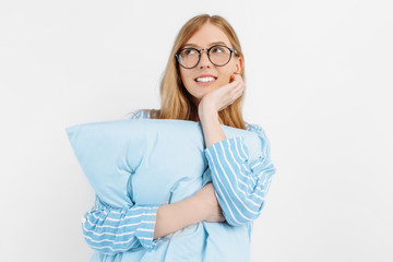 Beautiful young girl in blue pajamas, with a pillow to sleep, posing on a white background