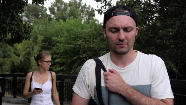 Difficult relations. Mad man walking while his girlfriend walking behind using the phone.
