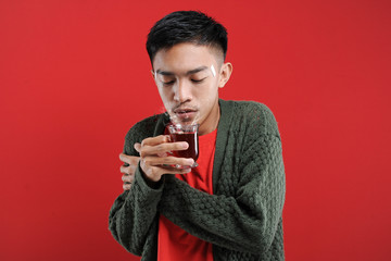 Sick cold and headache Young Asian man wearing a sweater while drinking hot tea