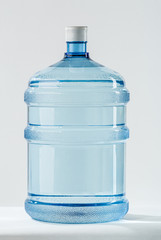 Big Blue Transparent Pet plastic water bottle for the cooler. 19 liter or 5 gallon refillable plastic water BPA Free jug dispenser. Mineral water delivery for offices. Studio shot on white background.