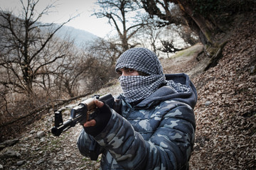 Naklejka premium Silhouette of man with assault rifle ready to attack on dark toned foggy background or dangerous bandit holding gun in hand. Shooting terrorist with weapon theme decor