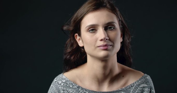 Attractive brown-haired woman in casual clothing looking at camera with serious facial expression over dark background. Concept of real human emotions