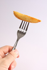 A studio photograph of a cooked oven chip on a fork