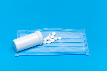 medical mask with a bottle of a medicinal product with a scattered pile of pills for the treatment of the respiratory tract of the lungs on a blue background with copy space.