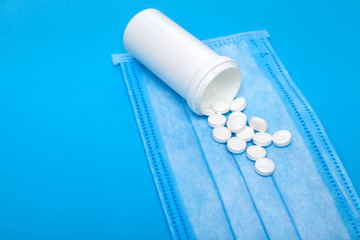 mock up medical mask with a bottle of a medicinal product with a scattered pile of pills on a blue background with copy space.