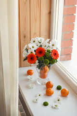 Vase with flowers and orange fruits near the window