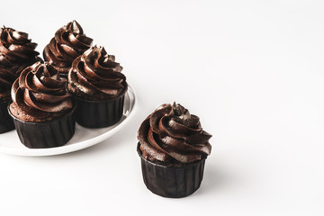 Delicious chocolate cupcakes with chocolate icing and sprinkled gold sparkles on white porcelain plate on isolated white background. Mockup for your design. Close-up. Place for text.