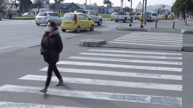A woman walking at a traffic crosswalk wearing a face mask